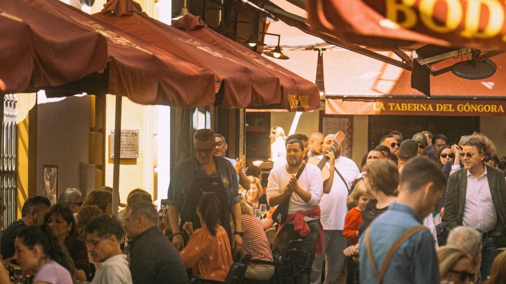 Terraço de restaurante movimentado em Sevilha, com clientes, músicos e mesas ao ar livre.