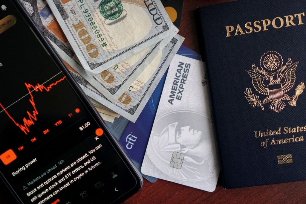 Passaporte, cartões, dinheiro e smartphone com aplicativo financeiro, representando serviços de investimento e operações financeiras digitais.
